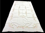 Toalha de mesa em tecido claro, ricamente decorada com bordados florais em tons de rosa e verde, formando delicadas guirlandas ao longo das bordas e composição central. Apresenta acabamento com barra ondulada. Medidas: 2,95 x 1,60 m.