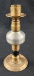 Castiçal em bronze, de estrutura robusta e pesado. Base circular, haste torneada com volumes geométricos e pátina natural do tempo, peça datada do século XX. Apresenta sinais de uso compatíveis com a idade. Medindo: 22 cm.