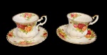 Royal Albert - Bone China. England. Duas xícaras em porcelana inglesa, com decoração floral policromada, delicado motivo de rosas em tons de vermelho, rosa e amarelo, entremeadas por folhagens verdes, aplicada sobre fundo branco. Bordas com filete dourado, No verso, marca da manufatura. Medidas: Xícara: 7,5 cm (altura) x 6,5 cm (diâmetro da boca) x 9,5 cm (largura com alça). Pires: 12,5 cm de diâmetro. As xícaras encontram-se em bom estado geral. Um dos pires apresenta quebra com restauro (colagem visível), conforme imagens. O outro pires sem avarias estruturais aparentes, apenas marcas compatíveis com o uso e o tempo.