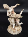 Escultura em porcelana esmaltada e policromada representando jovem e querubim, com ricos detalhes. Manufatura no verso. Medindo: 14 x 9 cm