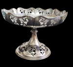 Antiga fruteira / centro de mesa confeccionada em metal espessurado a prata, com elegante decoração rendada vazada em todo o bojo e base, apoiada sobre haste central, apresentando desenho clássico. Medidas: 16 x 23 cm