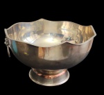 Champanheira confeccionada em metal espessurado a prata, de formato bojudo com borda ondulada e elegante, apoiada sobre base circular, apresentando alças laterais em forma de argolas com mascarões decorativos. Medidas: 19 x 32 cm.