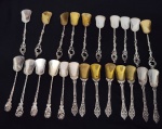 Lote composto por 23 colheres pequenas variadas, confeccionadas em metal espessurado a prata, com diferentes padrões de cabos ornamentados e conchas em acabamento prateado e dourado.