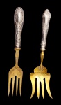 Par de garfos de servir, com cabos confeccionados em prata ricamente ornamentada em relevo, e hastes em metal dourado, apresentando desenho clássico e elegante, com detalhes gravados nas partes funcionais. Medidas: 25 cm de comprimento.