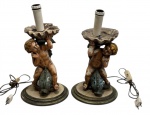 Par de abajures em madeira entalhada e policromada, representando figuras de putti (querubins) apoiados sobre elementos naturalistas ( peixes), sustentando o bocal superior. Peças de caráter decorativo, com rica composição escultórica e acabamento pintado à mão.Acompanham parte elétrica antiga (recomenda-se revisão). Não possuem cúpulas. Medidas: 41 x 22,5 cm.