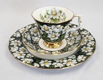 Royal Albert, England - Trio de chá em porcelana inglesa Bone China, padrão `Mountain Aven` da coleção Provincial Flowers, datado de 1975. Apresenta exuberante decoração floral com margaridas brancas sobre fundo preto e branco realçadas por filetes dourados nas bordas. O conjunto é composto por xícara, pires e prato de sobremesa. Manufatura no verso. Prato mede: 20,5 cm. Em ótimo estado.