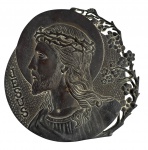 Placa devocional antiga, em metal patinado, com relevo representando o perfil de Jesus Cristo, halo circular e inscrição JESUS CRISTO. Apresenta borda vazada com decoração floral e suporte traseiro articulado, permitindo apoio sobre superfície.Peça de caráter religioso, com belo trabalho em relevo e pátina do tempo, ideal para coleção ou decoração sacra. Mede 18 cm.
