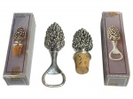 METAL PRATEADO, lote com duas (2) peças, sendo: A) 1 abridor de garrafas e B) 1 tampa com acabamento em cortiça, confeccionadas em metal espessurado a prata no formato de pinha, cinzelado por cachos e folhagens, acondicionadas em caixa original, possivelmente sem uso.