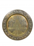 METAL DOURADO, um (1) prato decorativo em metal dourado, com representação do Taj Mahal ao centro, ricamente ornado com motivos florais e inscrição comemorativa em torno da cena, medindo 24,5cm.
