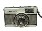 FOTOGRAFIA, uma (1) máquina fotográfica Olympus Trip 35 (marca japonesa fundada em 1919, notabilizada pela produção de equipamentos ópticos e câmeras de ampla difusão no século XX), em metal e material sintético, com objetiva Olympus D. Zuiko 1:2.8 f=40mm. Peça apresentando sinais do tempo e marcas de uso. Sem garantia de funcionamento.
