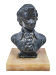ESCULTURA, um (1) busto de Wolfgang Amadeus Mozart, confeccionado em bronze com patina escura, apoiada sobre base quadrangular em mármore italiano, medindo 16x10x10cm. Possui fio de cabelo na base.