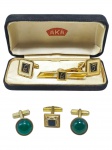 INDUMENTÁRIA, conjunto com três (3) peças: 1 par de abotoaduras e 1 prendedor de gravata, confeccionado em metal dourado, compondo conjunto acondicionado em estojo original AKA, com aplicações em esmalte nas cores preto e branco, monogramados. Acompanha ainda três abotoaduras avulsas em metal dourado, sendo duas com aplicação verde em formato circular e uma quadrangular de rochedo, apresentam sinais de uso, verdes com falhas na douração.