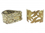 BIJUTERIAS, dois (2) braceletes, confeccionados em metal dourado, sendo: A) 1 com esmaltagem de tom dourado, decorado por formas abstratas em relevo, apresenta sinais de uso, medindo 7x5,5cm e B) 1 decorada por folhagens em vazados com realces em vermelho, medindo 6x5cm, ajustável.