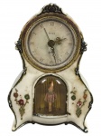 RELÓGIO, um (1) relógio de mesa da marca RENSIE (marca de relojoaria associada à produção de relógios decorativos de pequeno porte, com modelos voltados ao uso doméstico e ornamental), em caixa de material sintético ornamentado em tom marfim, com mostrador circular, numeração romana, ponteiros trabalhados e compartimento frontal com figura de bailarina sob cúpula plástica, apresentando decoração floral em relevo, sinais do tempo, desgastes, oxidações e marcas de uso. Sem garantia de funcionamento, medindo 15x10,5x4,5cm.