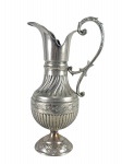 METAL PRATEADO - (1) Grande jarra confeccionada em metal espessurado à prata , corpo em caneluras e gomos torcidos , bico vertedor alongado, alça lateral vazada em desenho sinuoso e pé circular ornamentado em relevo com motivos florais. Medida : 40 x 21 cm