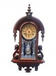 RELÓGIO ANSONIA (tradicional fabricante norte-americana de relógios, fundada em 1851, em Connecticut, Estados Unidos, destacando-se pela produção de relógios de parede, mesa e estante no século XIX e início do século XX), um (1) relógio de parede, com caixa confeccionada em madeira, apresentando frontão arqueado, elementos torneados e laterais recortadas, aplique de cabeça de Minerva, mostrador circular com numeração romana e dois furos para corda, porta frontal envidraçada com decoração e visor para visualização do pêndulo. Apresentando sinais do tempo, desgastes no mostrador e marcas de uso. Usado, não testado e sem garantia de funcionamento. Porta solta, bilro colado e com bicado, medindo -70x33cm.