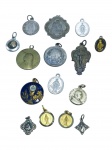 ARTE SACRA, quinze (15) medalhas e pingentes religiosos, em metais diversos, com representações devocionais variadas, incluindo Virgem Maria, crucifixo, santos e símbolos eucarísticos, alguns exemplares com esmaltação. Lote com peças de diferentes formatos e tamanhos, apresentando sinais do tempo, uso, desgastes, oxidações e perdas pontuais, maior medindo 3,5x2cm e menor 1cm.