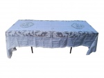 CAMA, MESA & BANHO, uma (1) toalha de mesa retangula, confeccionada em tecido na tonalidade branca, com aplicações rendadas e ornatos figurativos em medalhões e faixas laterais, apresentando motivos florais e querubins. Peça apresentando marcas de guardado e rasgos, vide foto, medindo 334x168cm.