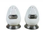 PORCELANAS, duas (2) peças, sendo: A) 1 saleiro e B) 1 pimenteiro, confeccionados em porcelana na tonalidade branca em formato de ovo, com placa e base em estanho com gravação SAL e PIMENTA, medindo 7,5cm de altura.