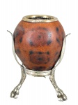 METAL PRATEADO, uma (1) cuia para chimarrão confeccionada em cabaça e borda em PRATA DE LEI, borda gravada A. L. O. D. e também na base, confeccionada em metal espessurado a prata da manufatura CORNETA, sobre três pés finalizados em garras, medindo 13,5x8,5cm.