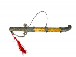 CUTELARIA, uma (1) espada oriental decorativa com bainha, apresentando empunhadura e guarda em metal dourado ricamente ornamentado, bainha com decoração marmorizada, ponteiras em metal trabalhado, corrente de suspensão e borla em fios vermelhos. lâmina em aço inox com gume, porém, necessita amolar, medindo 50cm de comprimento.