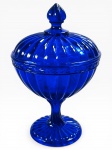 VIDRO, uma (1) compoteira dita GOMINHO, confeccionada em vidro na tonalidade azul cobalto, faixa moldada por folhagens e pega da tampa no feitio de pinha, haste gomada apoiada sobre base circular, medindo 21x13,5cm.
