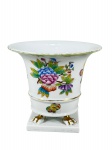 HEREND (Fundada em 1826 na vila de Herend (próxima ao lago Balaton, na Hungria) por Vince Stingl), um (1) vaso confeccionada em porcelana hungara na tonalidade branca, decorado por flores, folhagens e borboletas em policromia, apoiada sobre base quadrangular com pés em garra, filetes e realces em douração apresentando falhas e bicado na borda, medindo 13x15cm.