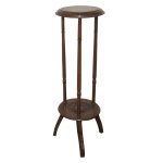 Mesa lateral para dois estágios na forma de coluna em madeira. Tampo circular sustentando três colunas retas com leves detalhes. Pés levemente recurvos. Brasil. Séc. XX. 92 x 29 cm.