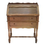 Pequena Secretaire a abattant em madeira clara, encimada por galeria. Tampo retangular escavado com reserva ondulada, revelando interior com 3 gavetinhas e compartimento. Caixa reta apresentando frente com par de gavetões superpostos. Pernas torneadas e retilíneas, ornadas por anelados e carreteis. Base com amarração em H. 107 x 81 x 41 cm (fechado). 107 x 81 x 70 cm.