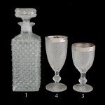 Conjunto de Licoreiro em cristal, translucido de formato quadrangular chanfrado e lapidado. 22 x 9 cm. Acompanham 7 taças em vidro translucido decorado no estilo bico de jaca: Borda prateada.  16 cm (4 taças). 14 cm (3 taças).