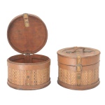 Par de caixas circulares com tampas reclináveis, construídas em madeira clara e lisa. Apresentam laterais trançadas em junco. Tampas no estilo, com cintas transversais e alças superiores. 20 x 24 cm.