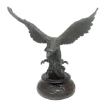 Escultura em petit bronze patinado, representando águia de asas abertas e garras à frente. Base circular em degraus. 55 x 70 x 40 cm.
