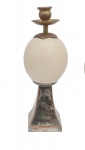 DUE SORELLE - Castiçal italiano montado com ovos de avestruz sobre base em metal dourado no formato de pirâmides. Haste superior encimada por pratinhos e bobeches em metal polido. Marcas nas bases. 30 x 10 cm.