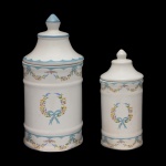 Conjunto de 2 potes para toucador em cerâmica artesanal da manufatura nacional Luiz Salvador, Itaipava. Apresenta formato cilíndrico de superficie branca decorado com guirlandas com laços de fita e frisos, predominando a cor azul. Marca da manufatura no verso. 28 x 12 cm. e 20 x 9 cm. Peças sem uso.