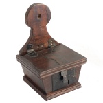 Brasil. Séc. XVIII - Esmoleira das Almas em madeira lisa, de formato retangular com laterais levemente inclinadas. Bordas duplas e caneladas centralizando grande fecho em ferro. Suporte superior recortado em corneta e encimado por adorno circular. 30 x 20 x 18 cm.