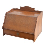 Séc. XIX - Escrivaninha de viagem possivelmente inglesa, em carvalho claro. Caixa retangular com tampo reclinável revelando prateleiras. Laterais recortadas e salientes, encimadas por frontão ondulado, centralizando adorno arqueado e apoiadas em pés lisos. Parte inferior com gaveta e chave. 30 x 38 x 28 cm.