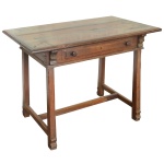 Brasil. Séc. XIX - Mesa retangular rústica em madeira maciça, com tampo liso e saliente, e borda canelada. Saia reta apresentando gavetão almofadado, ladeado por colunatas recurvas. Pernas retilíneas, reunidas à base por amarração em H, e rematadas por pés recortados e revirados. 78 x 103 x 61 cm.