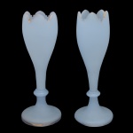 Par de elegantes floreiras em opalina monocromática de cor azul celeste. Bojos alongados no formato de tulipas, rematados por bordas dentadas e douradas, apoiados em anelados. Bases circulares lisas. 28 x 11 cm.