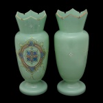Par de vasos em opalina verde água, ornamentados à frente por medalhões policromados ovalados, decorados com frisos interrompidos por estilizações centralizando florões. Bojos cônicos, encimados por gargalos em corneta rematados por bordas dentadas. Bases circulares lisas. Assinaturas e numerações soba as bases. 26 x 10 cm.