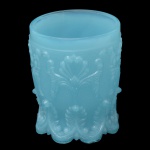 Copo formato cilíndrico em vidro moldado de cor azul celeste, profusamente ornamentado por folhagens, florões e volutas em alto relevo. Bojo reto com borda circular lisa. Base levemente esparramada e recortada por pequenos arcos. Base côncava decorada por filetes espiralados, centralizando rosácea de mesmo estilo. 10 x 8 cm.