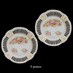 Conjunto de 9 pratos em porcelana, com bordas onduladas e margens fenestradas, interrompidas por coroas de louro e estilizações douradas. Fundos ornados por arranjos florais policromados. 17 cm.