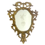 Espelho de parede no formato de escudo, emoldurado por galhos floridos e vazados em madeira dourada. Apresenta ao centro cena acetinada com figura de Diana caçadora, a deusa da caça com seu arco e flecha, símbolo da independência feminina, de pé sobre pedestal. 70 x 50 cm.