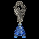 Elegante perfumeiro em cristal com bojo azul safira, moldado no formato de pedra facetada. Exuberante tampa transparente, acetinada e vazada, apresentando dançarina com véu realçado por flores e estilizações. 23 x 8 x 8 cm.