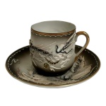 Xícara e Pires Japoneses com Dragão em Relevo. C. 19301960. Conjunto composto por xícara e seu pires em porcelana japonesa, ricamente decorado com representação de dragão em relevo, símbolo tradicional de força e proteção na cultura oriental. Apresenta acabamento em policromia com fundo em degradê e detalhes em douração, evidenciando o trabalho manual e o refinamento decorativo da peça. Base com marca em vermelho contendo o caractere  (prosperidade), comum em peças japonesas de exportação do período. Exemplar inspirado na tradição decorativa do estilo Kutani, datado de meados do século XX.