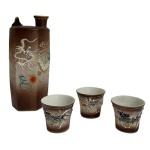Conjunto Japonês de Saquê em Porcelana. Dragão em Relevo. C. 19401960 - Conjunto composto por garrafa (tokkuri) e três copos (ochoko) em porcelana japonesa, ricamente decorados com representação de dragão em relevo, símbolo tradicional de força e proteção na cultura oriental. Apresenta acabamento em policromia com fundo em degradê, além de detalhes em douração, evidenciando o trabalho manual e o refinamento decorativo da peça.