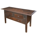 Meia cômoda rústica em madeira lisa, com tampo retangular saliente e borda canelada. Caixa reta apresentando par de gavetas à frente sobre gavetão. Pernas retilíneas de secção quadrangular. Puxadores torneados. 77 x 154 x 60 cm. Marcas de uso e do tempo.