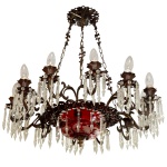 Importante lustre para 12 luzes em bronze e cristal. Cúpula inferior ornamentada em overlay de cor rubi com adornos florais, bordada por pingentes lapidados e rematada por coroa com borda dentada sustentando braços recurvos. Bobeches cônicas, apoiadas em pequenos pratos realçados por ponteiras facetadas e encimadas por velas. Correntes superiores reunidas ao topo por canopla circular vazada.70 x 70 cm. Falta pequeno pedaço do suporte de encaixa da peça de cristal.