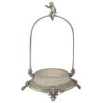 Centro de mesa em metal prateado. Colunas longas finalizadas com anjinho. 30 x 18 cm. Uma alça solta. Marca da manufatura no verso. Uma das alças solta.