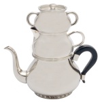 Wolf  Conjunto de 3 peças em metal prateado sobrepostas de manufatura nacional, sendo: bule com alça em madeira (9 x 17 cm), leiteira (6 x 10 cm) e açucareiro (4 x 10 cm). Falta a tampa.