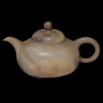 Pequeno e antigo bule chinês para chá, finamente esculpido em pedra de Shoushan, com tonalidades rajadas e mescladas em tons de cinza e amarelo. Destaca-se o perfeito encaixe da tampa, sem folga, e acompanhando os veios do bojo. Corpo globular achatado, com bico recurvo e alça em argola. Pequeno pé baixo com assinatura em laca de ouro do artista Feito por Xu Chun Feng, aluno do mestre Zhe Ming Zhi. Peça de coleção. 7,5 x 13,0 cm.